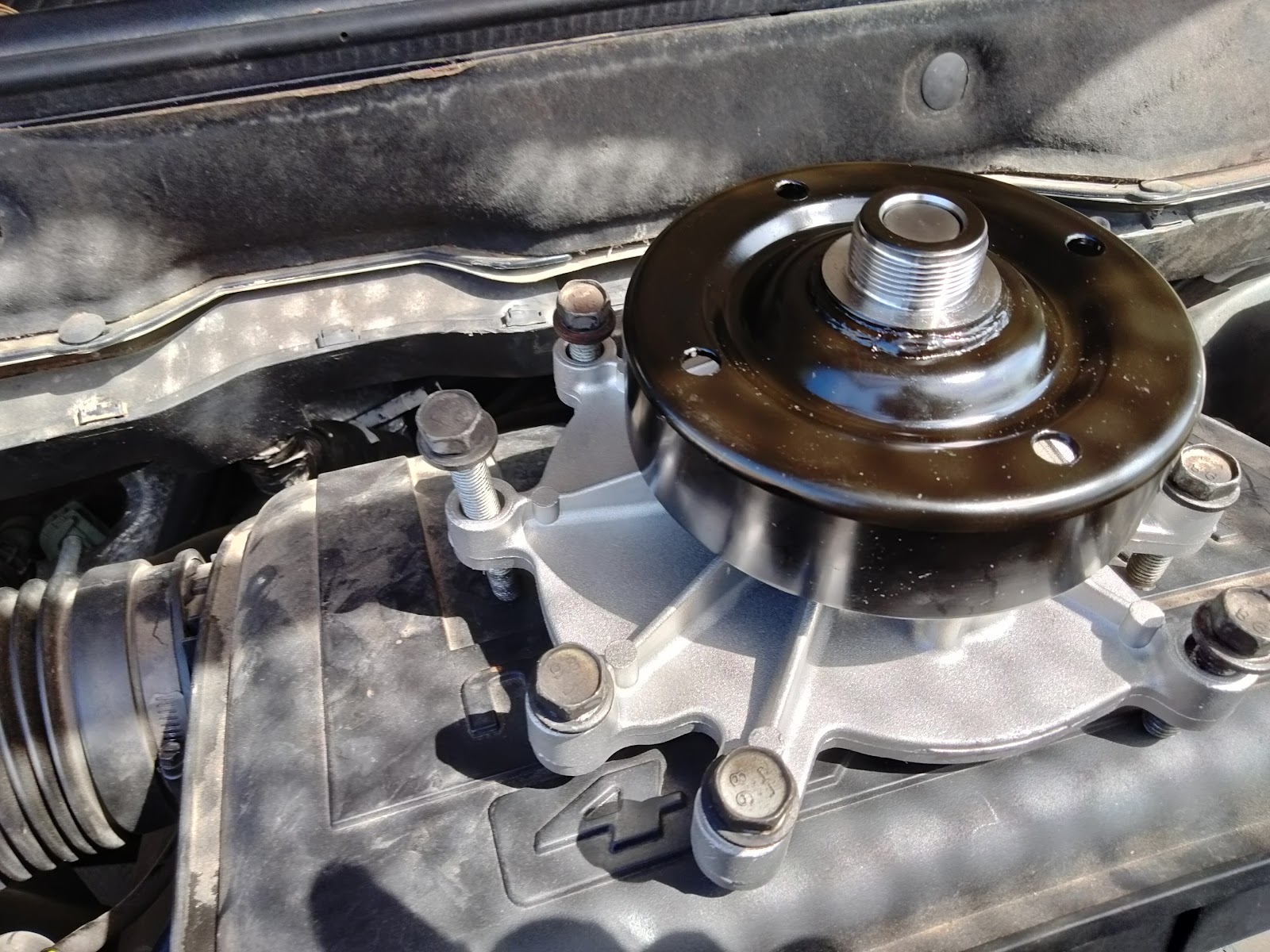 A new water pump with black pulley bolted onto the engine