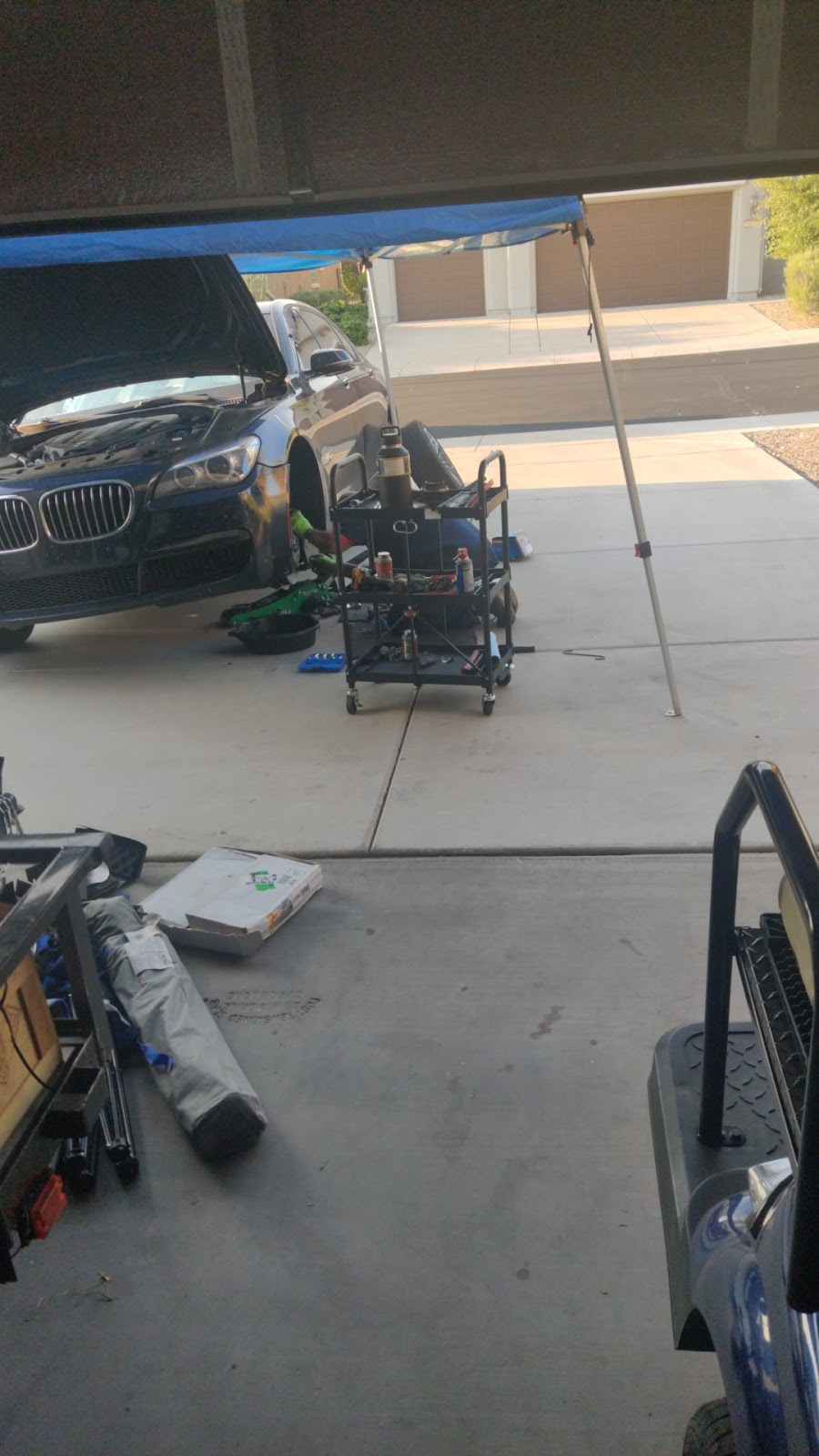 Blue canopy set up over a sedan with its hood open in a customer's driveway, rolling tool cart beside it