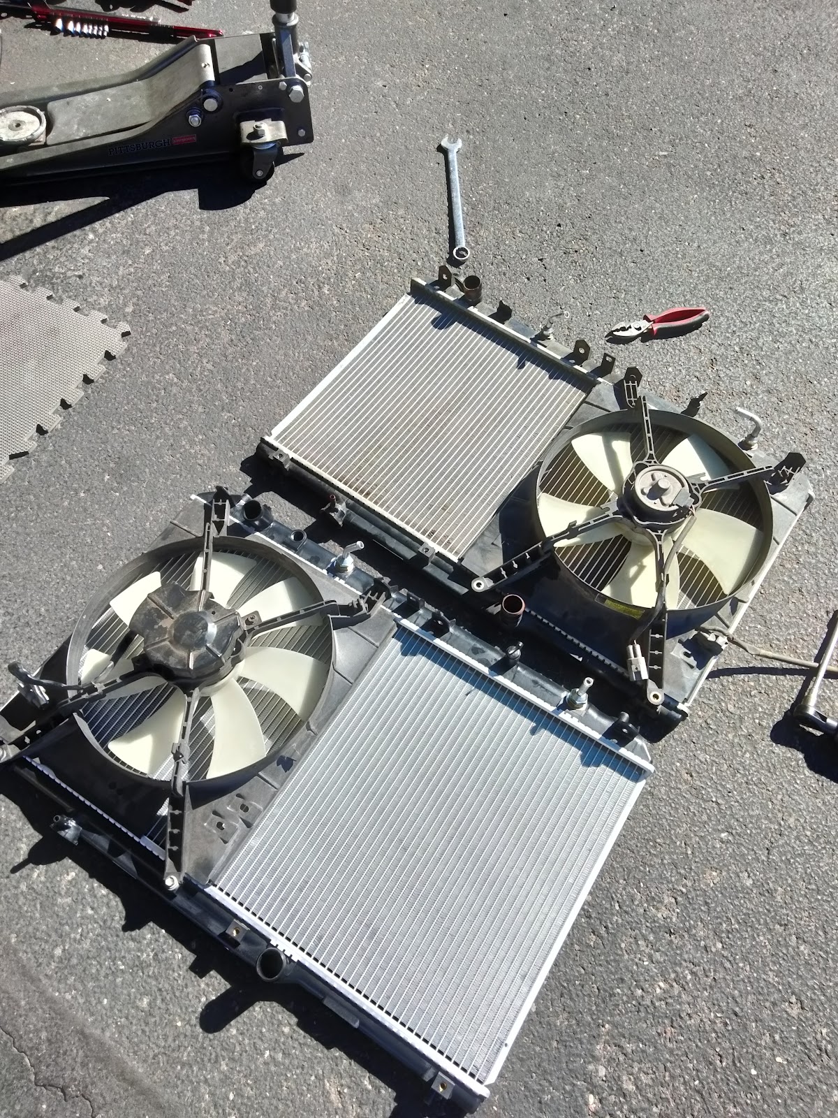 Radiator and fan assemblies laid out on the pavement beside a floor jack
